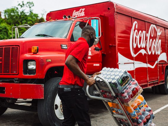 A Caribbean Bottling Company driver loading cases from a Coca-Cola delivery truck
