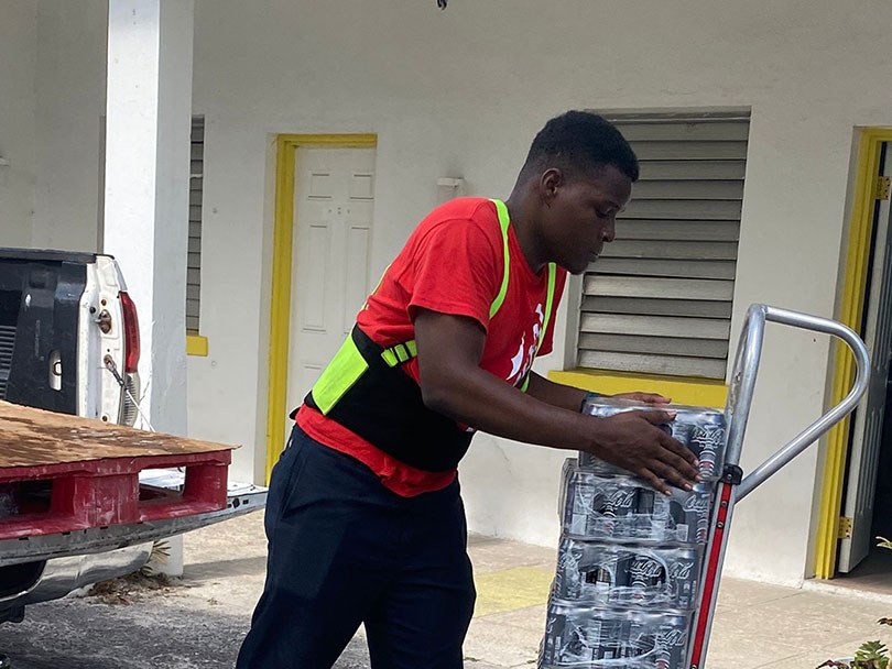 A Caribbean Bottling Company driver delivering cases to a customer